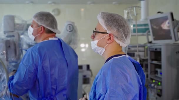 手術室にいる外科医 医療用ユニフォームとマスクの医師は クリニックでロボットシステムを含む操作を行います 医療コンセプト — ストック動画