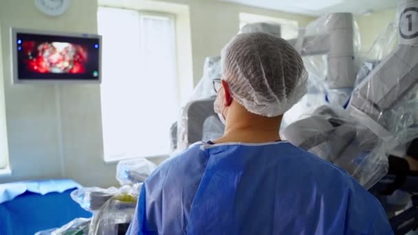 ドクターは外科手術でモニターを調べる 病院で医療用ロボットを使った現代手術 リアビュー — ストック動画