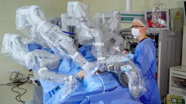 ハイテク機器による手術 外科ロボットは 患者に対して最小限の侵襲的手術を行います 病院のロボットマシン近くの医療ユニフォームの専門外科医 — ストック動画