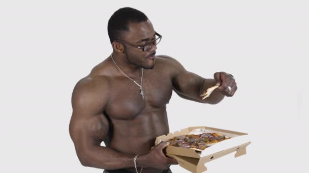 アフリカ系アメリカ人がピザを食べる カートンのパッケージから美味しいピザを楽しむ黒い筋肉男性 スポーツマンはスタジオで孤立した不健康な食べ物を食べる スローモーション — ストック動画