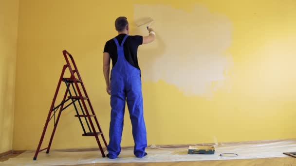 身穿蓝色工作服的男人用滚子粉刷墙壁 工人用一种新的颜色装饰房间 绘画服务 后视镜 — 图库视频影像