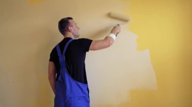 Boyacı yenileme odasının içinde boya silindiri var. Genç inşaatçı odada duvar boyuyor. İşçi dairede renk değiştiriyor. Arka görünüm.