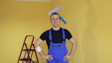 İçerideki bir ressamın portresi. Tulum giymiş, kafasında bir boyacı silindiri olan ve baş parmağıyla evet işareti yapan genç bir işçi. Yenileme hizmetleri.