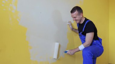 Odada tadilat yapan pozitif işçi. Gülen müteahhit boyayı açık renkli boyayla boyuyor. Oda makyajı..