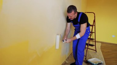 Yeni tarz yenileme. Üniformalı işçiler duvarları boya rulosuyla boyarlar. İnşaat tekeri duvarları boyuyor.