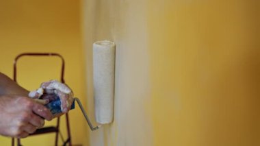 Oda tadilatı sırasında boya silindiriyle el ele tutuşmak. Duvarında beyaz renkli boya silindiri taşıyan bir adam. Profesyonel resim servisi. Yakın plan..