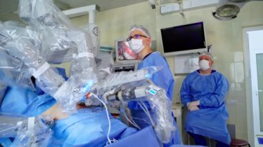 Ameliyat yapan robotik kollu yenilikçi ekipmanlar. Modern klinikte bir hastayı ameliyat eden tıbbi robot. Tıp üniformalı doktorlar robot sistemin çalışmalarını inceliyorlar..