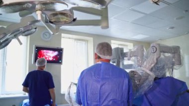 Modern klinikte minimal invazif ameliyat. Cerrahlar mikro cerrahisi modern robotik ekipmanların çalışması sırasında tıbbi monitörden gözlemliyorlar. Arka görünüm.