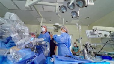 Tıpta yeni teknolojiler. Modern klinikte robotik cerrahi. Tıbbi robotun yanında üniformalı bir grup doktor hastaya mikro cerrahi uyguluyor..