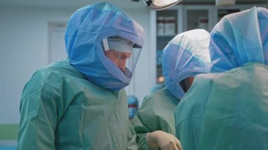 Koruyucu şapkalar konusunda uzmanlar klinikte çalışıyor. Güvenlik üniformalı bir grup doktor koronavirüs salgını sırasında ameliyat yapıyor..