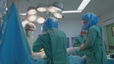 Pandemik zamanda ameliyat. Bir grup koruyucu üniforma uzmanı klinikte tıbbi lamba altında bir hastaya ameliyat yapıyor..
