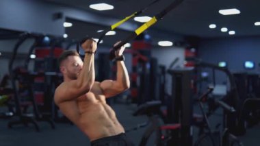 Spor salonundaki sporcu. Gömleksiz kaslı bir adam spor merkezinde prezervatifle simülatöre kaslarını pompalıyor. Vücut geliştiricisinin günlük çalışması.