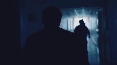 Ameliyathaneye hareket eden doktorların silueti. Hastane koridorunda yürürken sağlık görevlisi üniforması giyiyor. Arka plan.