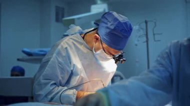 Doktorlar klinikte ameliyat yaparlar. Bir hastayı ameliyat ederken cerrahi aletlerle çalışan bir tıp uzmanı. Erkek asistan cerraha yardım eder.