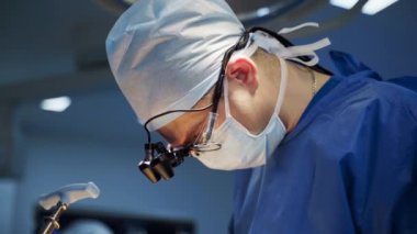 Maskeli profesyonel bir doktor ameliyat yapıyor. Ameliyat ışıkları altında cerrah, elinde tıbbi aletle bir hastaya ameliyat yapıyor..