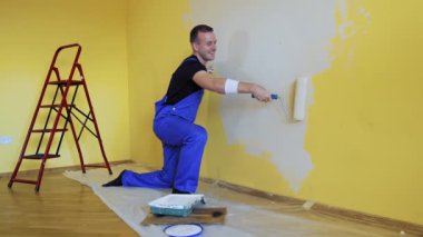 Mutlu erkek işçi duvar boyuyor. Boya silindirli profesyonel bir genç adam dairede eğleniyor. Oda boyama işi. Yenileme konsepti.