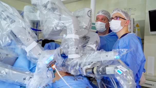 未来型ロボットの近くの医療用制服の医師 現代的なロボット機器による手術 操作を行うロボットアームを搭載した医療機器 クローズアップ — ストック動画