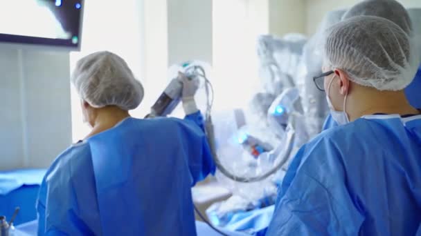 ロマを操作する医療専門家と外科ロボット 医用制服の医師は 外科手術のためにロボットアームを接続します バックビュー — ストック動画