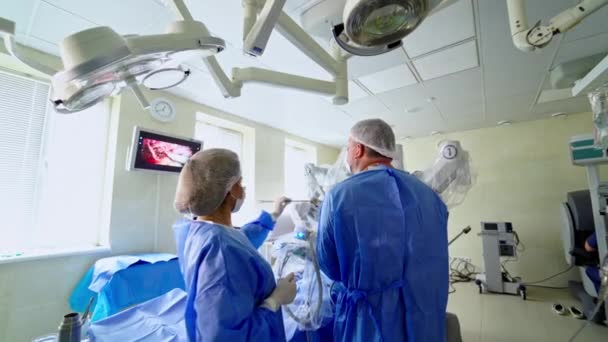 革新的な技術による手術 医療専門家は 診療所で外科的プロセスを持つ医療モニターの背景にあるロボット手術中に特別な機器を使用しています — ストック動画