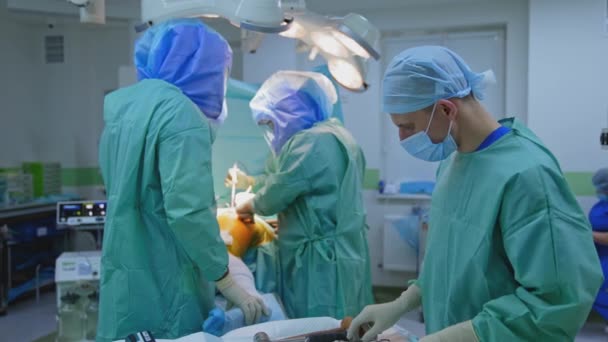 在危险病毒期间给病人做手术 在诊所进行手术的穿着防护服的外科医生的协同工作 化验室附近戴口罩的医疗助理 — 图库视频影像