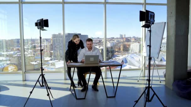 オフィスで一緒に働いている企業の同僚 ビジネスマンはテーブルに座り ラップトップに取り組んでいる 若い女性はビジネスで男性を助けます 窓から街の風景 — ストック動画