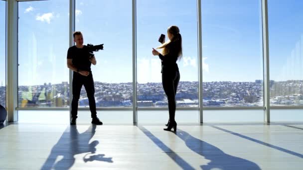 摄影师和一个在室内带电话的模特年轻女子在手机上自拍 而男子则用专业相机拍照 — 图库视频影像