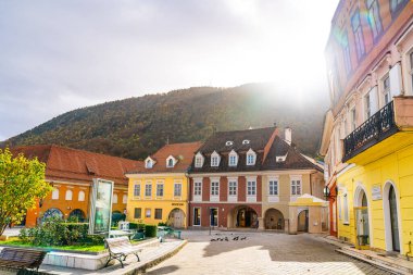 Romanya 'nın Brasov kentindeki binaların önündeki banklarda oturan bir grup insan. Çeşitli mimari yapıların dışındaki banklarda çeşitli bireyler oturuyor.