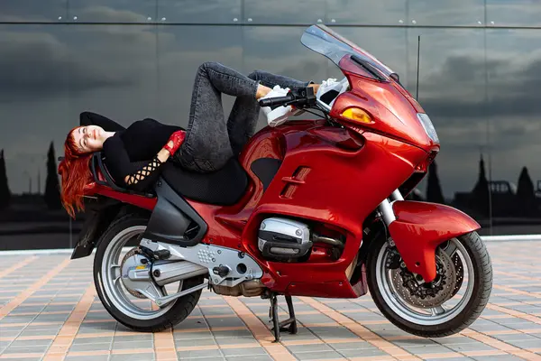 Woman Resting on Red Motorcycle. A woman comfortably lying on top of a vibrant red motorcycle.
