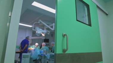 Plastik doktorlarla dolu bir ameliyathane. Kliniğin kapısındaki cerrahi odanın arka planı bulanık. Hastane koridorundan ameliyathaneye bak..