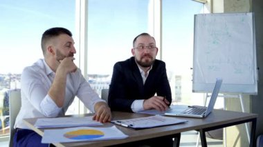 İki işadamı arasındaki konuşma. Başarılı girişimciler ofis merkezindeki masada oturur ve pencere manzaralı arka planda mutlu bir şekilde konuşurlar..