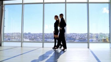 İş merkezinde yürüyen güzel genç kadınlar. İş kadınları şık siyah giyiniyor açık ofiste konuşuyor büyük pencereli ve şehir manzaralı.