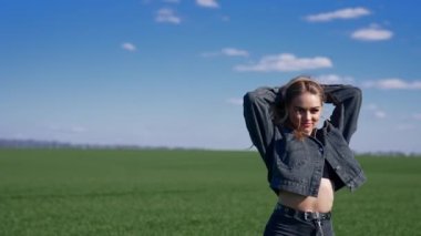 Sahada kanat çırpan saçları olan çekici bir model. Yeşil doğa arka planında yürüyen ve kameraya bakan gülümseyen genç bir kadın. Yavaş çekim.