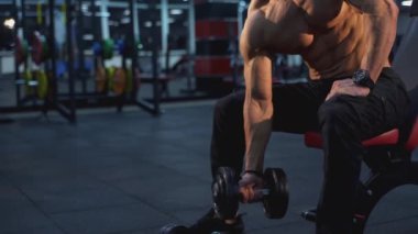 Atletik vücut egzersizi yapan yakışıklı bir adam. Dambıl kullanıyor. Gömleksiz sporcu, spor salonunda bisepsi şişiriyor..