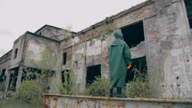 Terk edilmiş yerde koruyucu elbiseli bir adam. Güvenlik kıyafetli adam yıkılmış binaların arkasında tek başına duruyor. İnsan yok. Kıyamet kavramı.