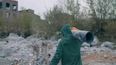 Güvenli giysili bir adam tehlikeli bölgede yürüyor. Koruyucu üniformalı ve solunum cihazlı insanlar kirli havayla dolu terk edilmiş bir yerde boru taşıyorlar. Arka görünüm.