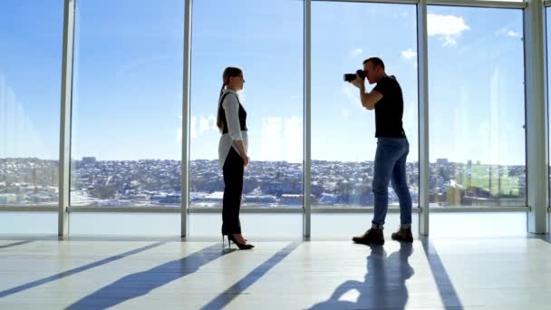 摄影师兼办公室女服务员 站在窗前时 一位戴眼镜的漂亮而优雅的女人在镜头前摆姿势 全景窗户与城市景观 — 图库视频影像