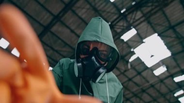Güvenlik kıyafeti ve gaz maskesi takmış bir kadının portresi. İnsan, antibakteriyel kostüm giyip terk edilmiş bir yerde eldiven eldivenle bir şeye dokunmaya çalışıyor. Gaz saldırısı..