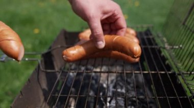 Adam ızgaraya sosis koyuyor. Açık havada ızgara taze et sosisi. Lanet sosisler kömürde kızartılır. Yakın plan..