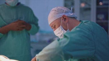 Estetik ameliyat. Ameliyat masasının yanında kendinden emin bir doktor duruyor. Kalifiye erkek cerrah sıkı plastik ameliyat yapıyor.