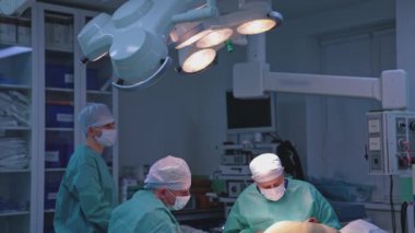 Cerrahlardan oluşan bir ekip ameliyathanede ameliyat yapıyor. Bir grup doktor hastanedeki tıbbi lambanın altında bir hastaya estetik ameliyat yapıyor..
