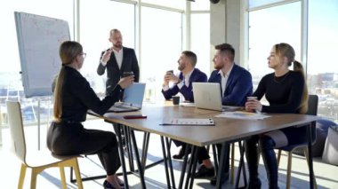 İş ortaklarıyla ofis odası. Bir grup genç girişimci masada oturup neşeli bir iş adamını dinliyor..