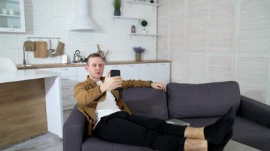 Genç adam web kamerası kullanıyor. Adam kanepede otururken video çekiyor. Yakışıklı erkek blogcu dairesinden görüntülü konuşma yapıyor..