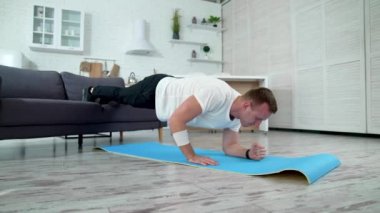 Genç adam evde antrenman yapıyor. Tecrit sırasında vücut şeklini korumak için sıkı egzersiz yapan yakışıklı bir adam. Karantina sırasında spor.