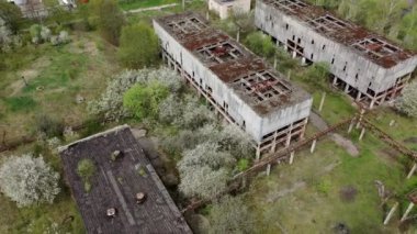 Çatılarında delikler olan yıkılmış fabrika binaları. Eski terk edilmiş sanayi tesisi. Yeşil doğa arka planında mahvolmuş bir üretim. Yukarıdan görüntüle.