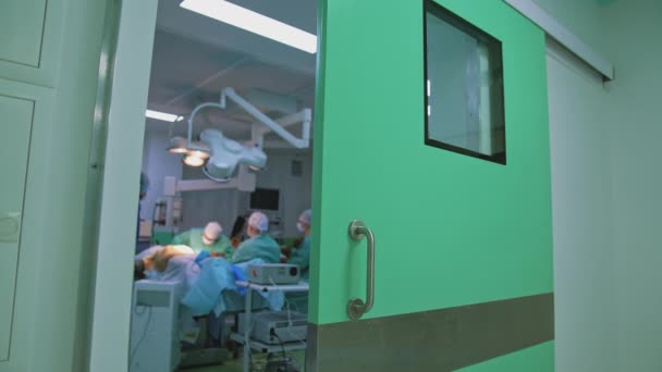 医療スタッフが手術を行っています 医療用ユニフォームの外科医のグループが手術を行っています 外科テーブルの患者さん 病院の廊下からの眺め — ストック動画