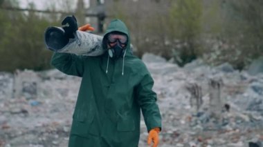 Radyasyon bölgesinde koruyucu giysi giyen bir işçi. Üniformalı ve gaz maskeli bir inşaatçı yıkılmış bir yerde boru taşıyor. Kimyasal saldırı.