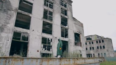 Radyoaktif bölgede biri var. Yıkılan binaların arka planında yürüyen kimyasal koruyucu giysili ve maskeli bir insan. Biyolojik saldırı.