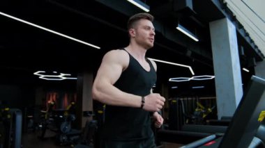 Genç yakışıklı adam simülatör eğitimi alıyor. Sporcu çocuk spor salonundaki modern bir koşu bandında koşuyor. Yavaş çekim.