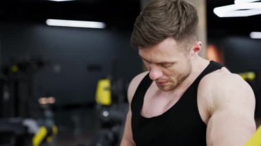 Antrenmandan sonra yorgun sporcu. Genç yakışıklı kaslı adam spor salonundaki simülatörün yanında duruyor ve dinleniyor. Sportif yaşam tarzı.