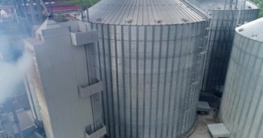 Tahıl asansörleri devrede. Duman içinde büyük metal ambarları. Modern endüstriyel bir fabrikanın gümüş alüminyum kapları. Hava görünümü.